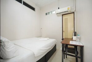 Hotellihuone, jossa on yksi sänky, työpöytä tuolilla, peili ja ilmastointilaite.