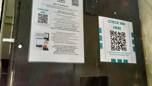 Uma porta de metal com dois códigos QR e instruções para hóspedes fazerem o check-in na Go Inn.