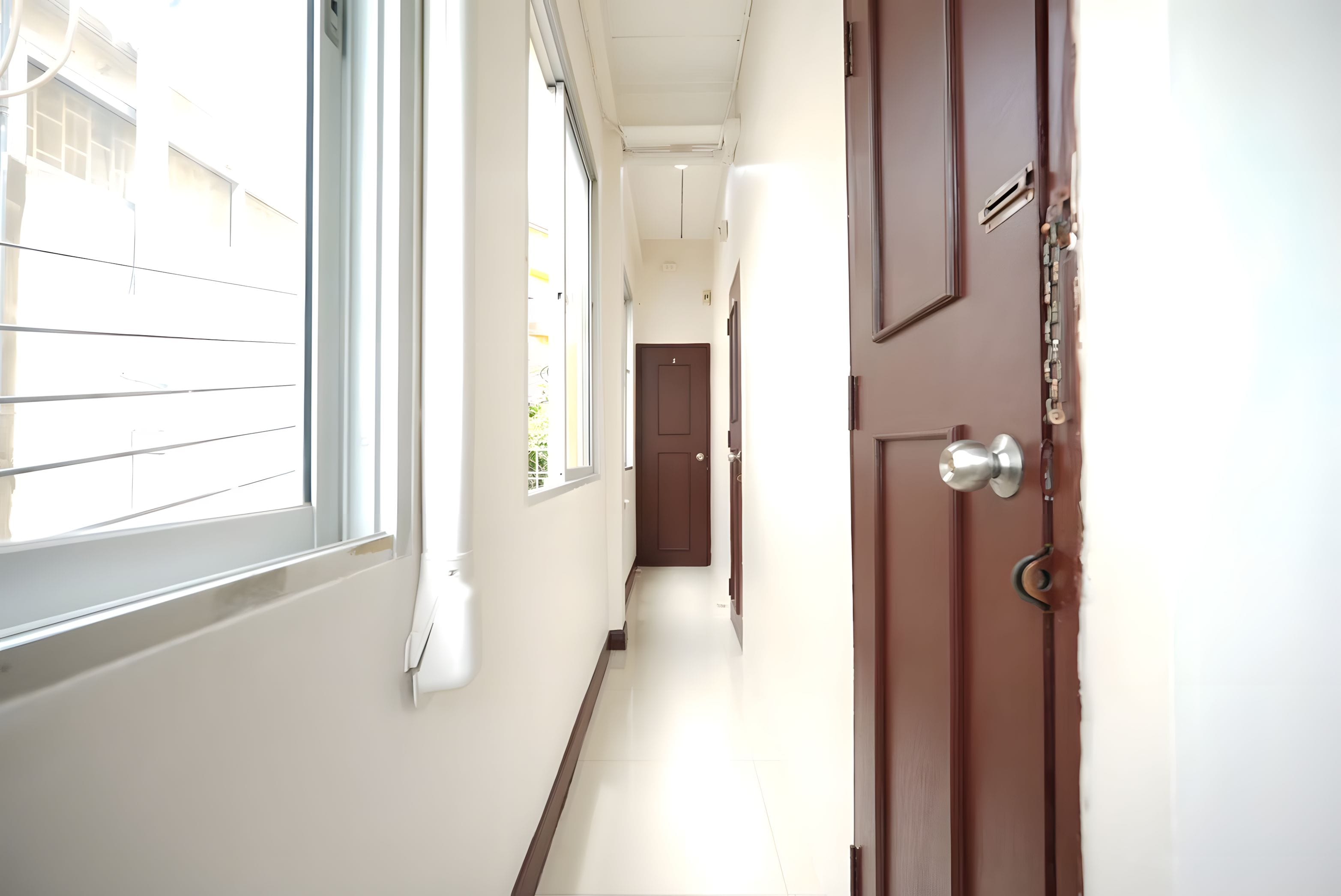 Um corredor com uma porta à direita, uma janela à esquerda e outra porta no final.