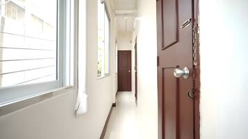 Um corredor com uma porta à direita, uma janela à esquerda e outra porta no final.