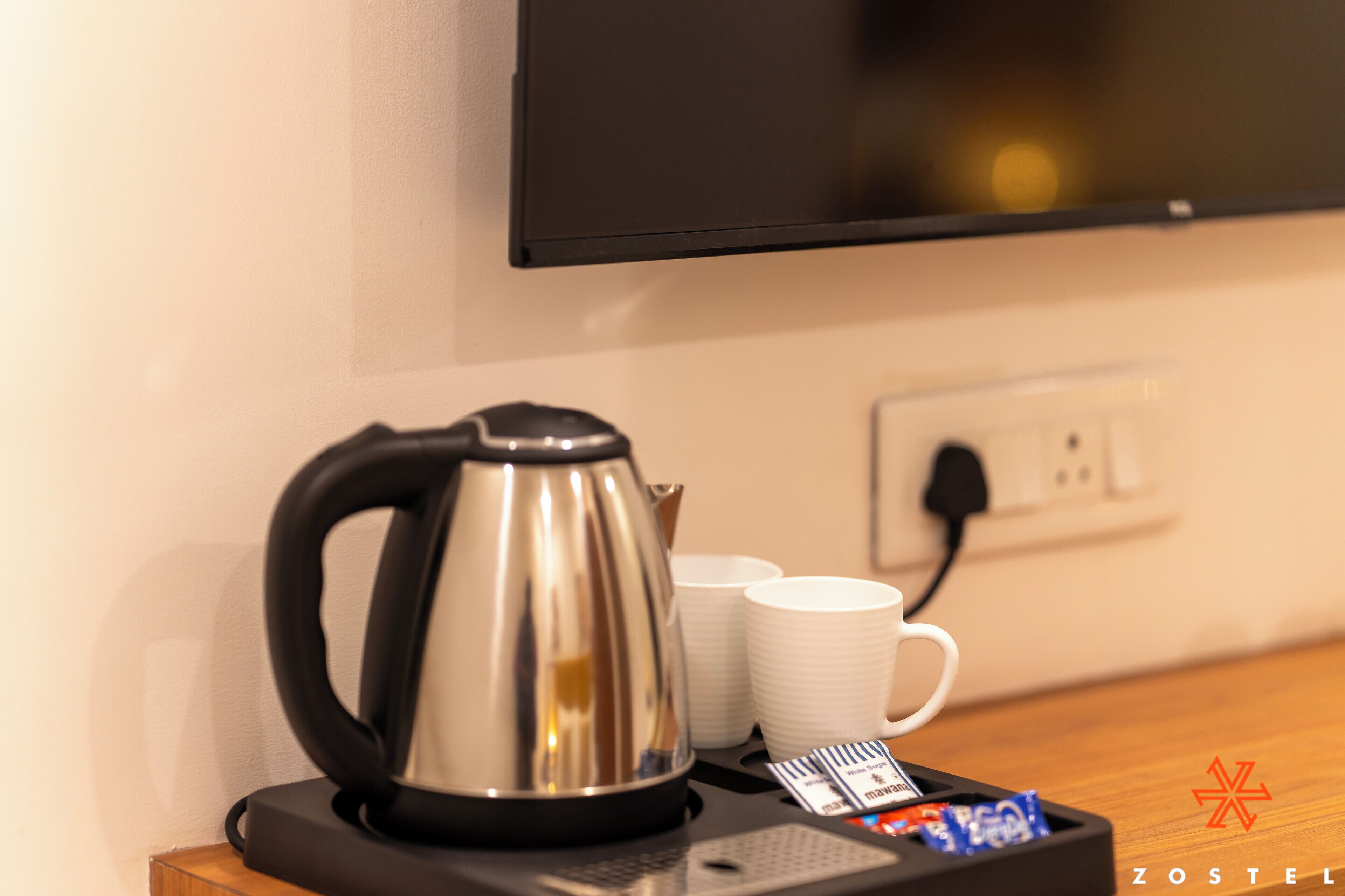 A kitchen area with a coffee maker, white mugs, and a power outlet.