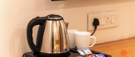 A kitchen area with a coffee maker, white mugs, and a power outlet.