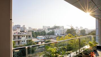 Un balcón con vista a un paisaje urbano, plantas en macetas y el sol brillando a través de la ventana.
