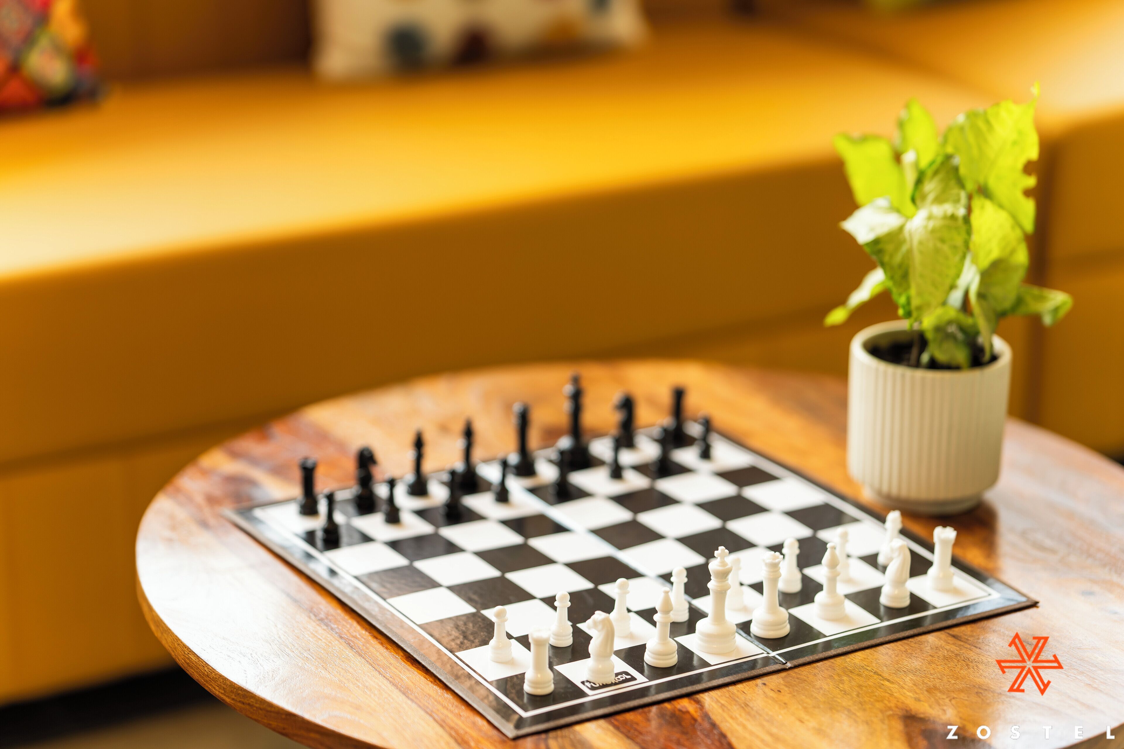 A chessboard on a wooden table with a potted plant beside it.