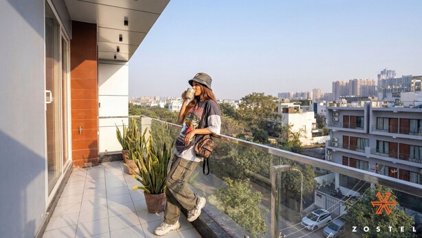 Una persona su un balcone con vista sulla città, una pianta in vaso e una ringhiera.