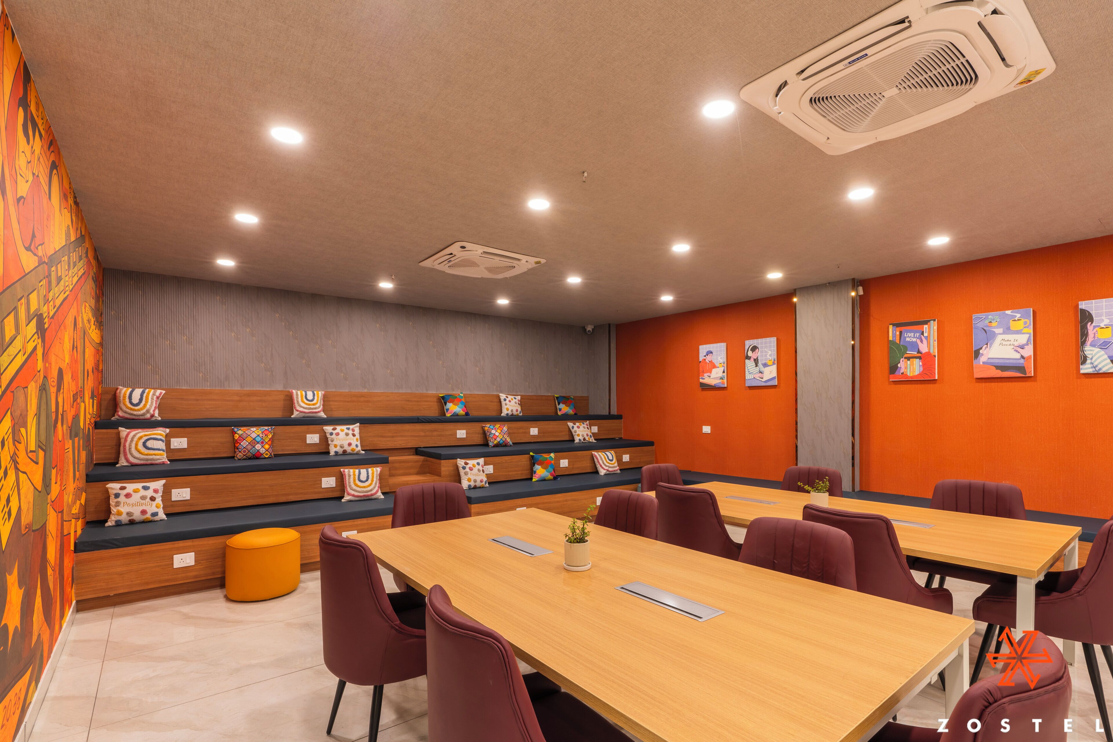A conference room with a long table, multiple chairs, a small orange stool, and a wall with colorful artwork.