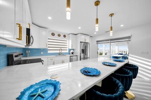 Een moderne keuken met witte kasten, een roestvrijstalen koelkast en een lang werkeiland met blauwe placemats.