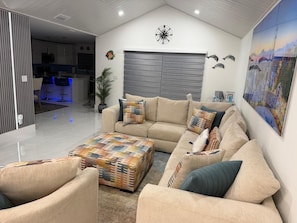 Un salon moderne avec un canapé beige, un pouf à motifs et un grand tableau représentant un pont.
