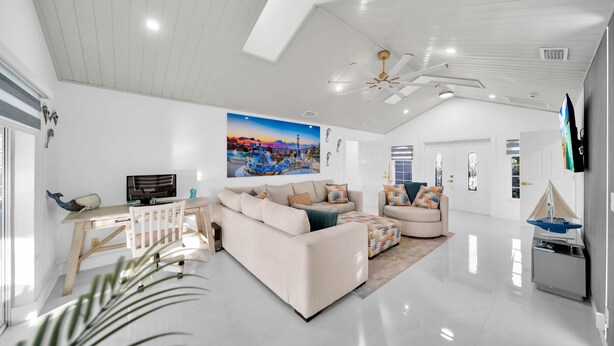 Ein geräumiges Wohnzimmer mit einer großen Couch, einem Couchtisch und einem Fernseher. Es gibt einen Deckenventilator und ein Bild an der Wand.