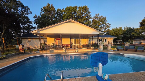 A swimming pool with a diving board, surrounded by a covered patio area with outdoor furniture.