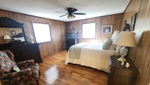 A bedroom with wooden walls, a bed with a white comforter, a dresser, a chair, and a ceiling fan.
