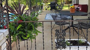 An outdoor patio with a covered seating area, a grill, and potted plants.