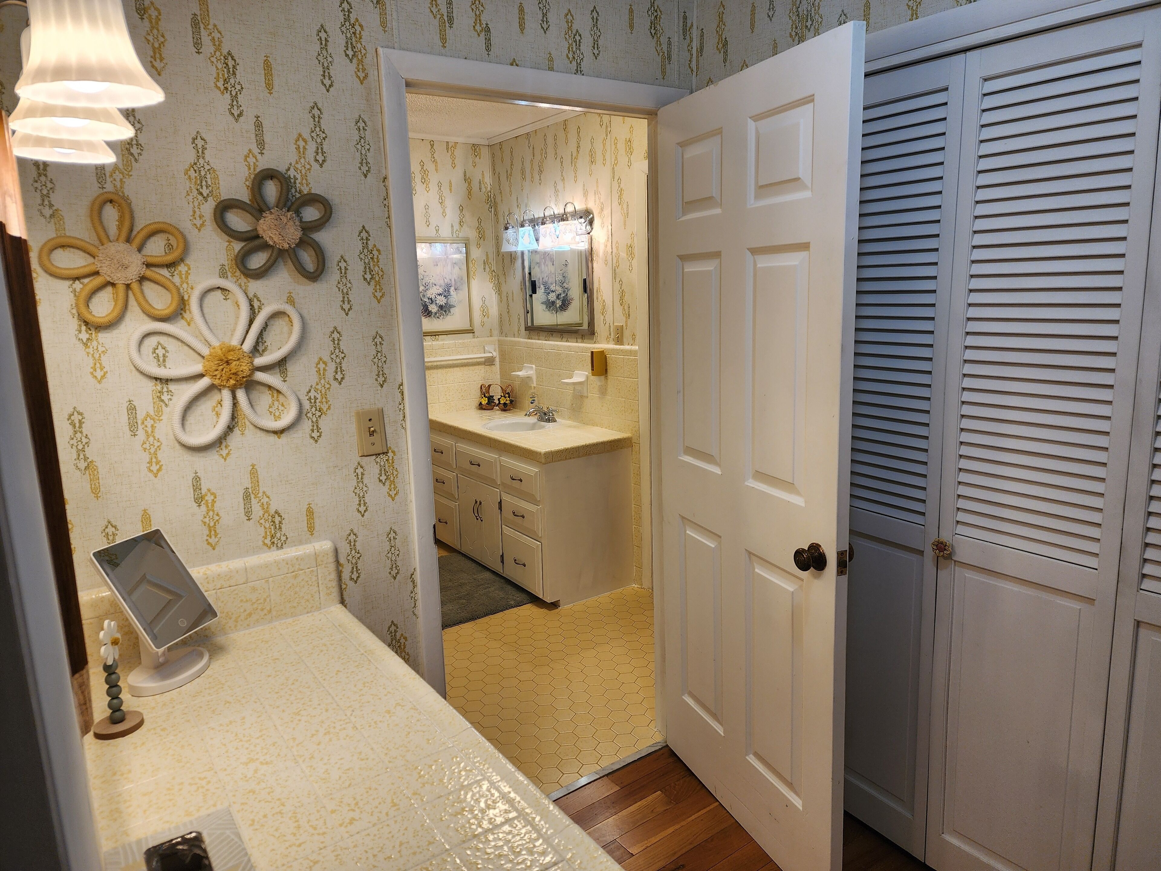 Une salle de bain avec un lavabo, un miroir et des toilettes. On y trouve également des décorations florales murales et un porte-rouleau de papier toilette.