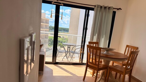 Een balkon met een tafel en stoelen, een schuifdeur en uitzicht op gebouwen en groen.