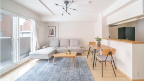 A modern living room with a sofa, a coffee table, and a dining area with chairs and a small table. - E-US NAEBO STATION 102 (Sapporo)