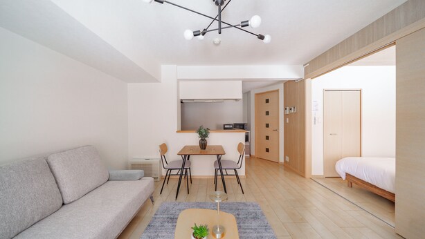 A modern living room with a sofa, a dining table with chairs, a small kitchen area, and a bedroom with a bed. - E-US NAEBO STATION 102 (Sapporo)