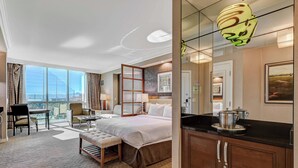 A hotel room with a large bed, a desk, a chair, a small table, a bench, a kitchen area with a stove, and a large window offering a city view. - MGM Signature-05-818 Accessible Studio (Las Vegas)