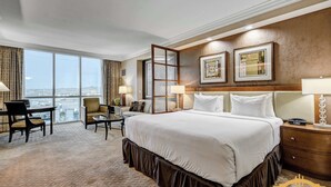 Ein Hotelzimmer mit einem großen Bett, einem Schreibtisch, zwei Stühlen und Blick auf die Stadt, mit gerahmten Bildern an der Wand.