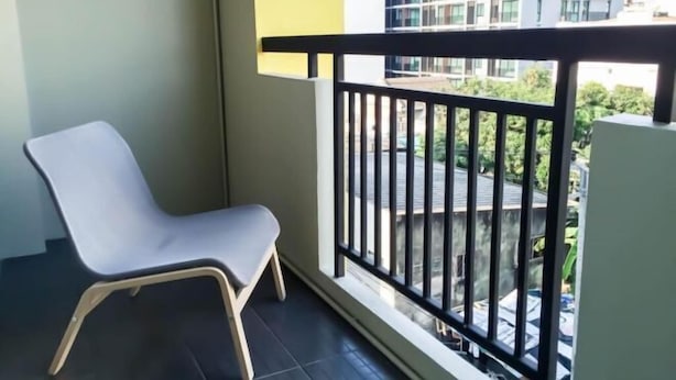 Un balcon avec une rambarde noire, une chaise grise et une vue sur un immeuble et de la verdure.