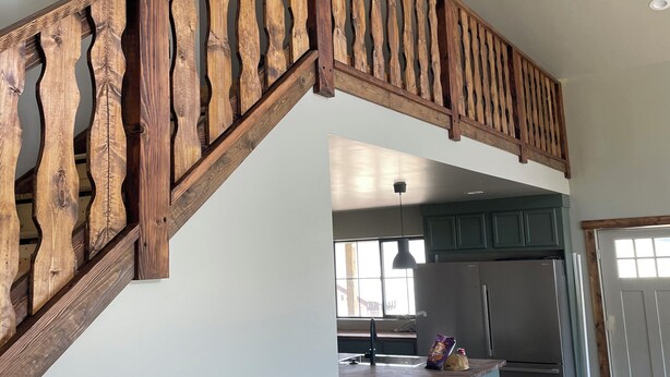 Una escalera de madera con un diseño único que conduce a una zona de cocina con refrigerador y ventana.