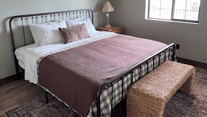 Un dormitorio con cama, mesita de noche, lámpara, ventana y ventilador de techo.