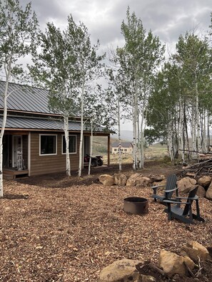A cabin with a metal roof, surrounded by birch trees and a view of a distant building. - Paradise Pines - Swap Screen Time With Family Time (Scofield)