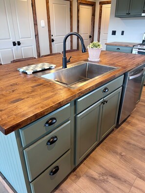 A kitchen with a wooden countertop, a stainless steel sink, and light green cabinets.