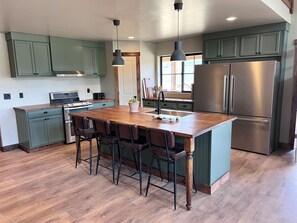 A modern kitchen with a central island, bar stools, a stainless steel refrigerator, and green cabinetry. - Paradise Pines - Swap Screen Time With Family Time (Scofield)