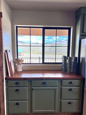 A kitchen with a window view of a landscape, wooden countertop, and green cabinets.