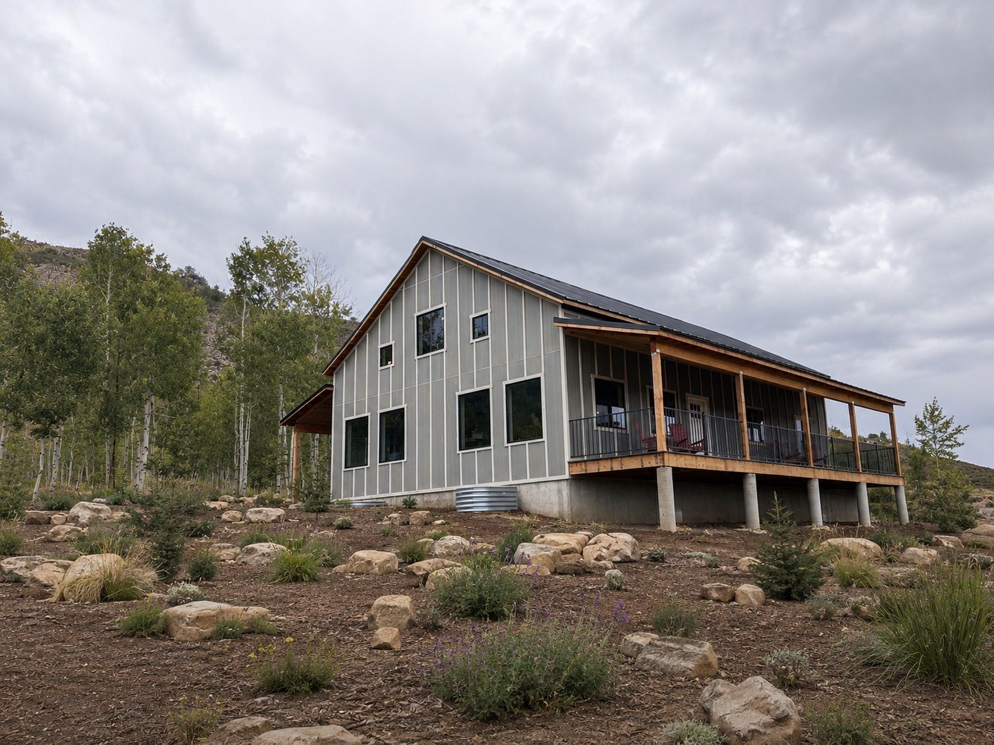 A modern two-story house with a balcony, surrounded by a natural landscape with rocks and sparse vegetation.