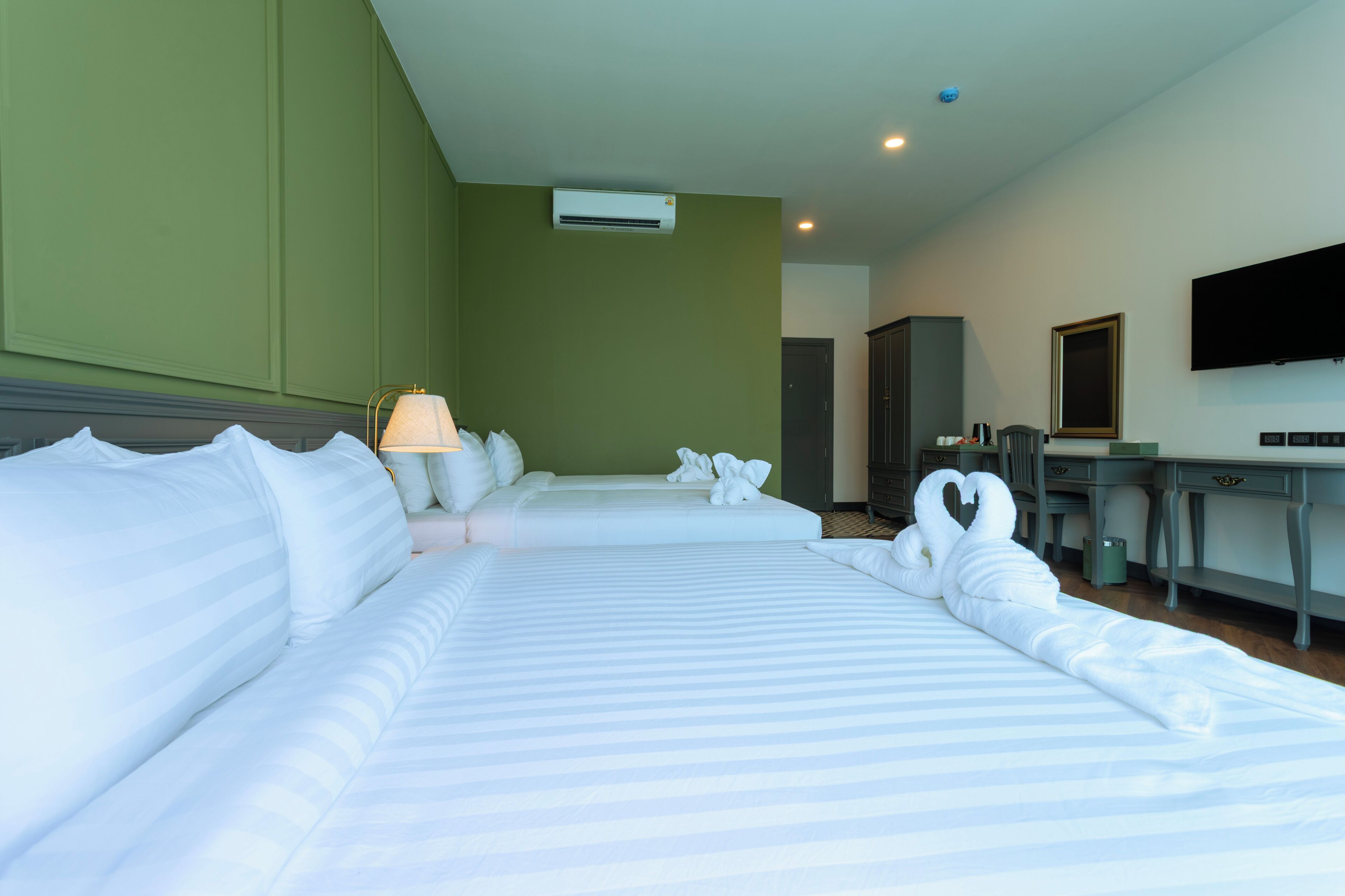 A hotel room with two beds, a desk, a lamp, an air conditioning unit, a television, and a mirror.