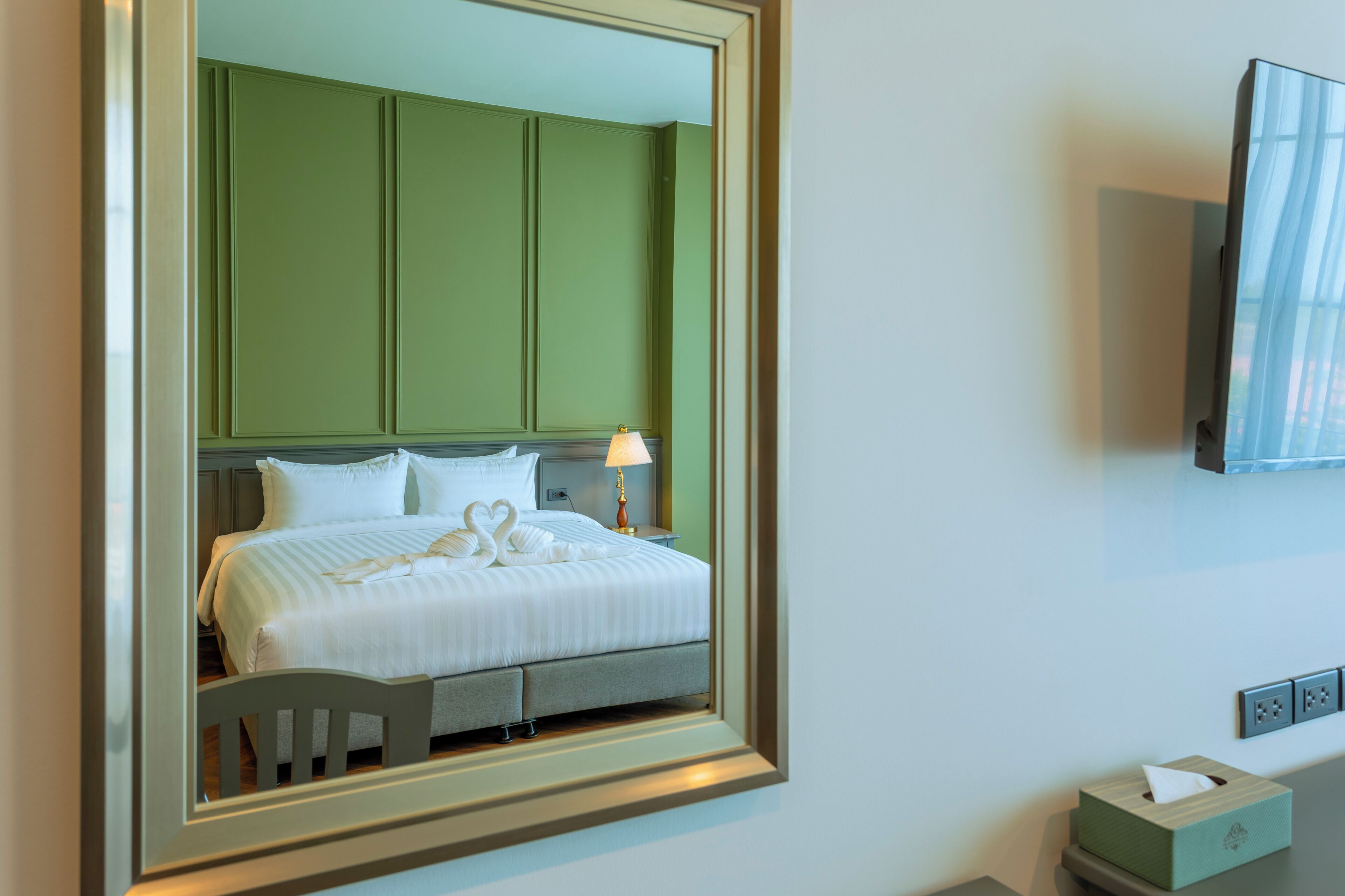 Una habitación de hotel con cama, mesita de noche, lámpara, espejo y televisión.