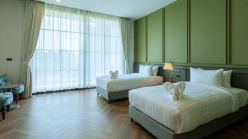 A hotel room with two beds, a table, and a window with sheer curtains.