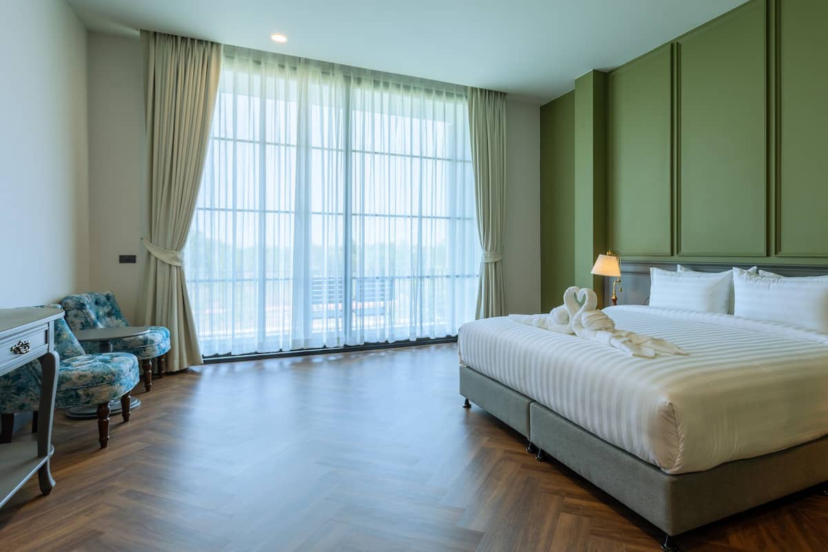 A hotel room with a large bed, a desk, two chairs, and a view through the window.