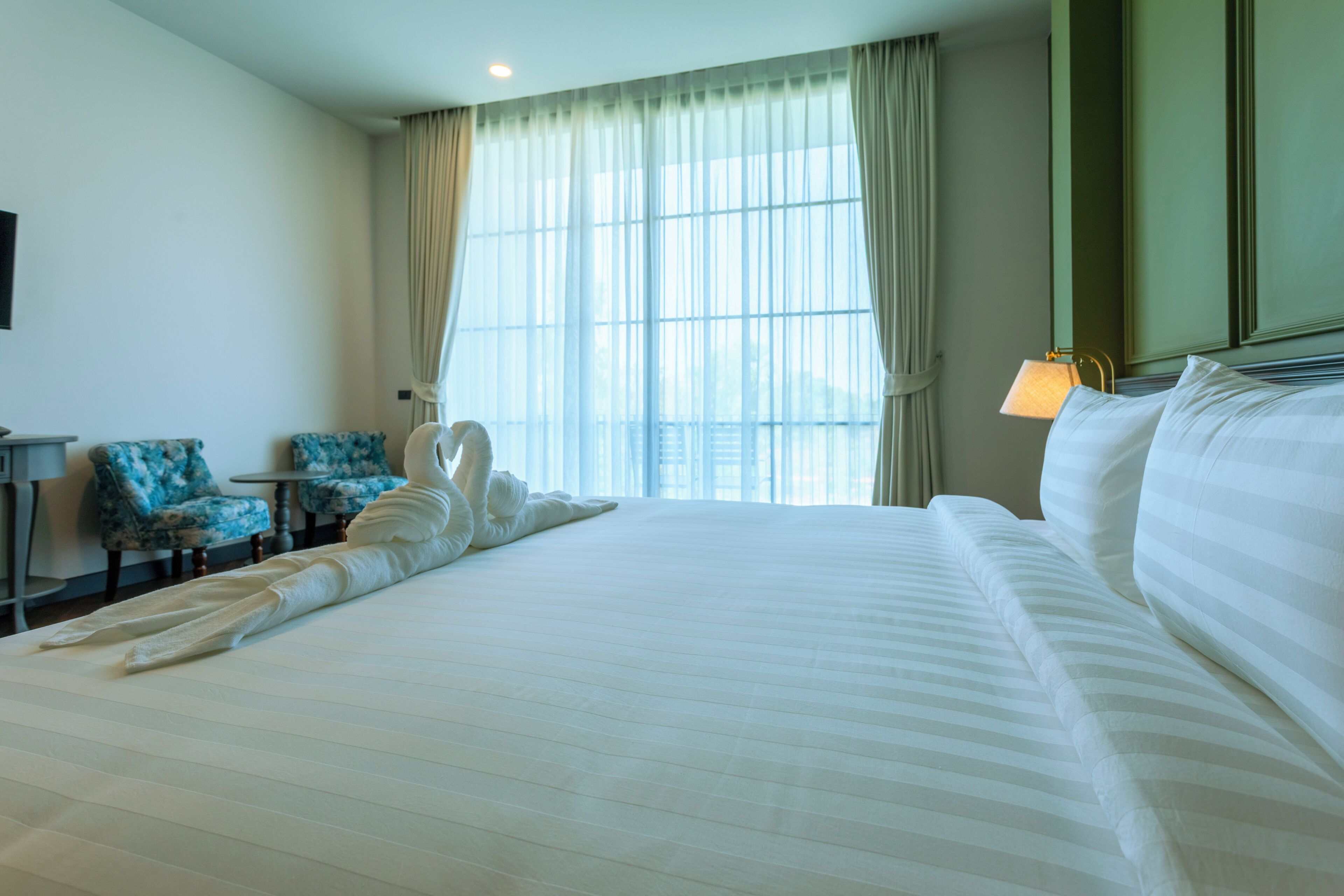 A hotel room with a large bed, a desk, two chairs, and a window with curtains.