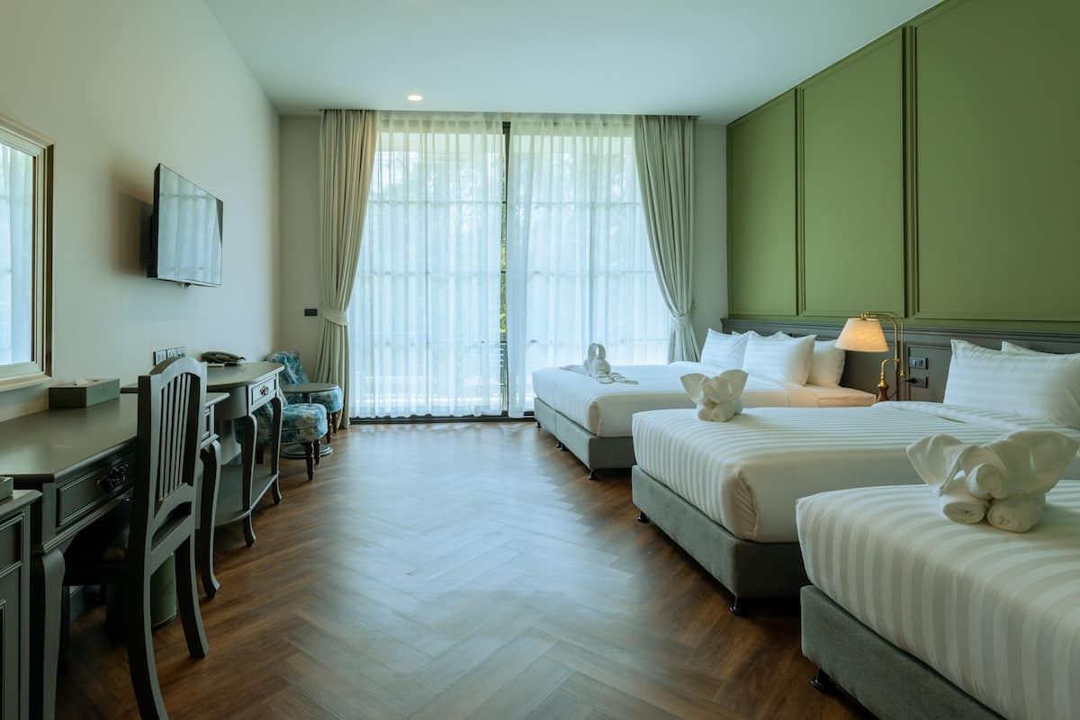 A hotel room with two beds, a desk, a chair, a TV, and a window with curtains.