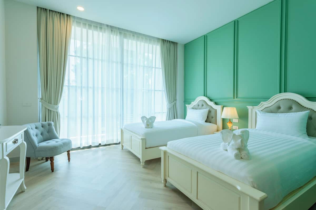 A hotel room with two beds, a chair, and a large window with curtains.