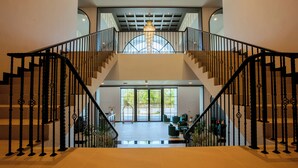 A spacious interior with a grand staircase, a chandelier, and a view through large windows. - Paradhevi Boutique (Ban Dung)