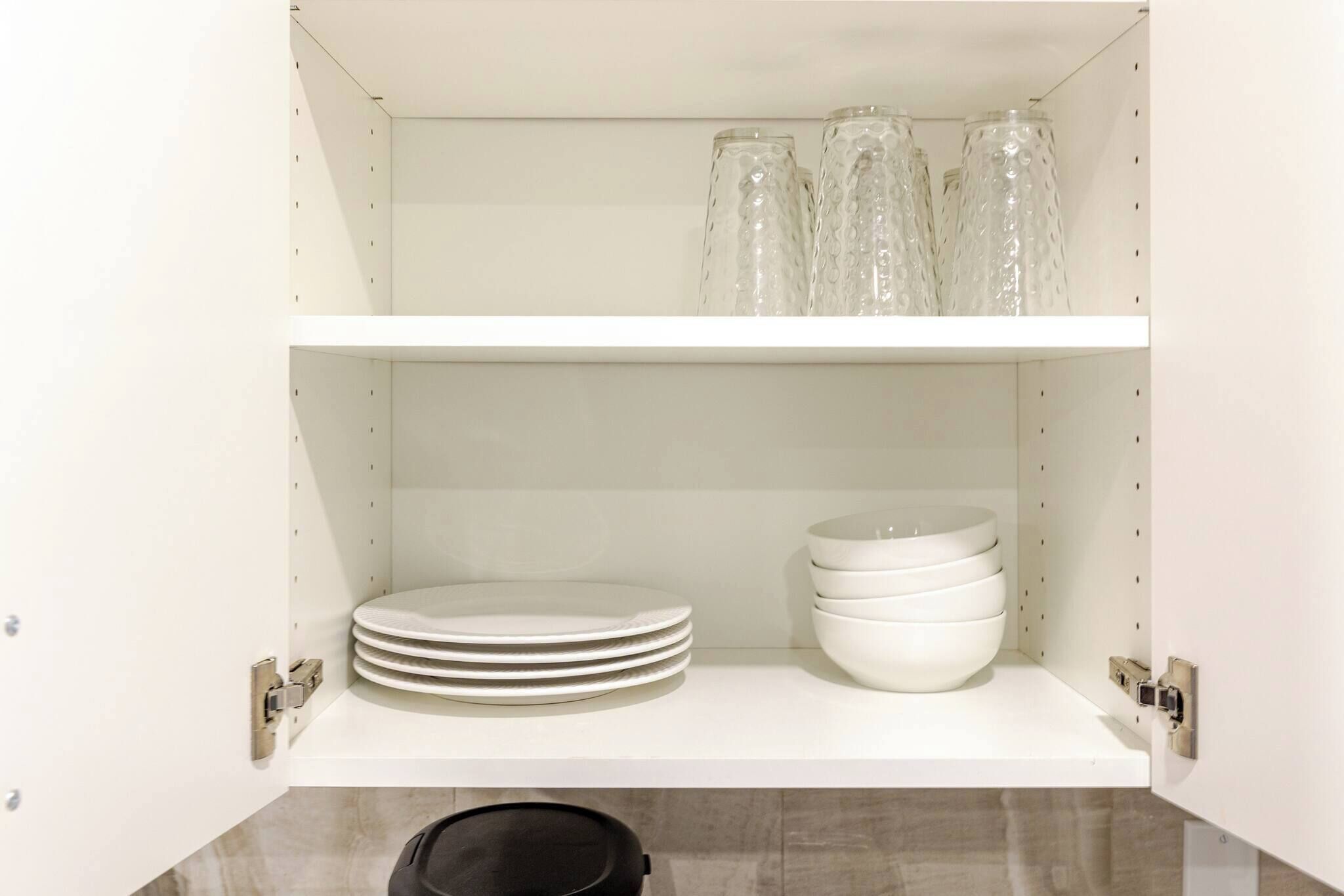 A kitchen cabinet with shelves holding stacked plates and bowls, and a black pot on the lower shelf.