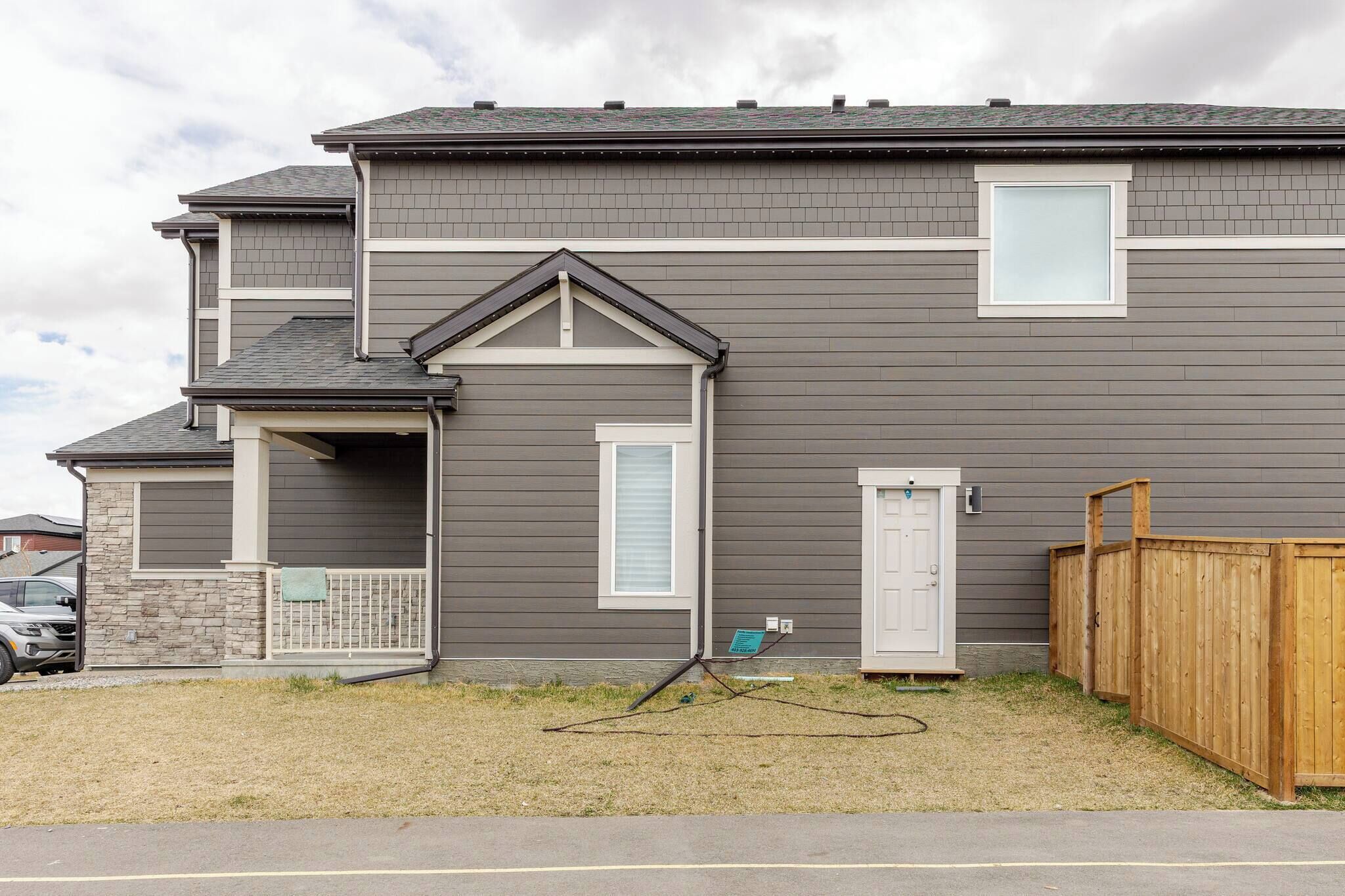 A two-story residential building with a grey exterior, a front porch, and a wooden fence.