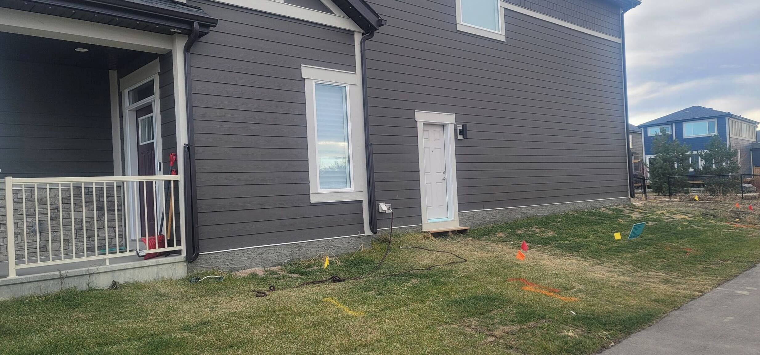 A residential house with a grey exterior, a front porch with a railing, a door, and a small window.