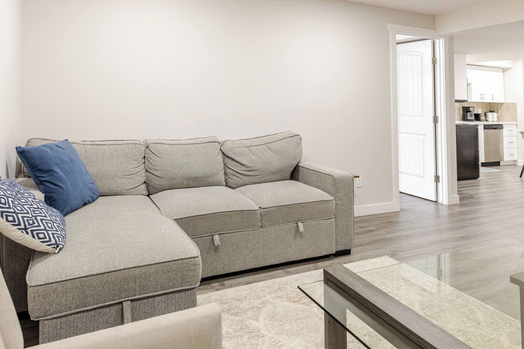 Uma sala de estar moderna com um sofá modular cinza, uma almofada estampada e uma mesa de centro de vidro.