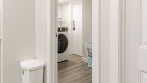 Une buanderie équipée d’un lave-linge, d’une poubelle et d’un panier à linge.