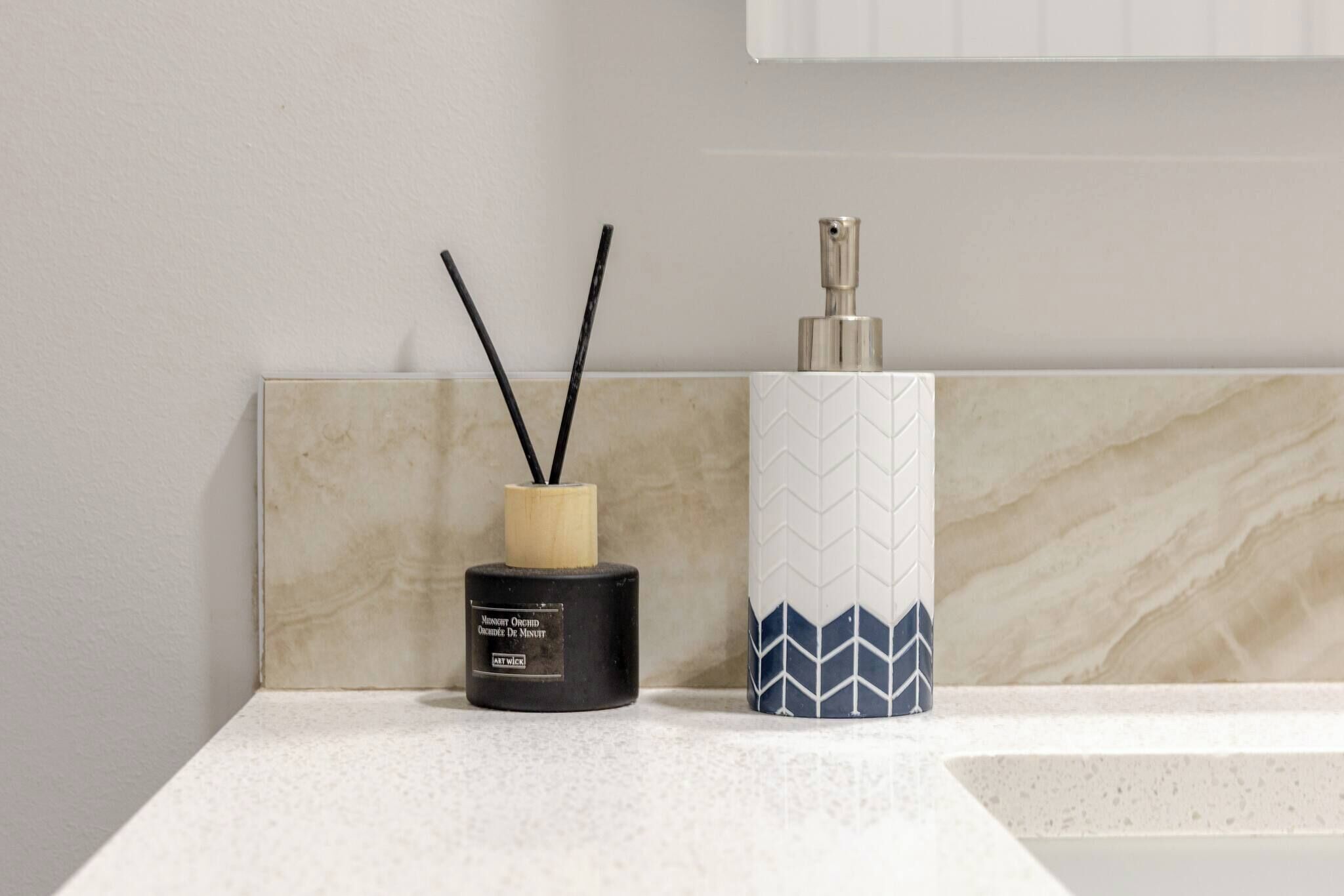 Tocador de baño con un difusor negro y un jarrón blanco con diseño azul.