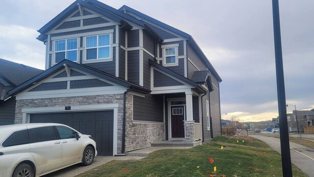 Une maison à deux étages avec un garage, une façade en pierre et une allée où est garée une voiture.