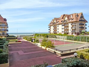 Edificio residencial con varios balcones, cancha de tenis y vista al mar.