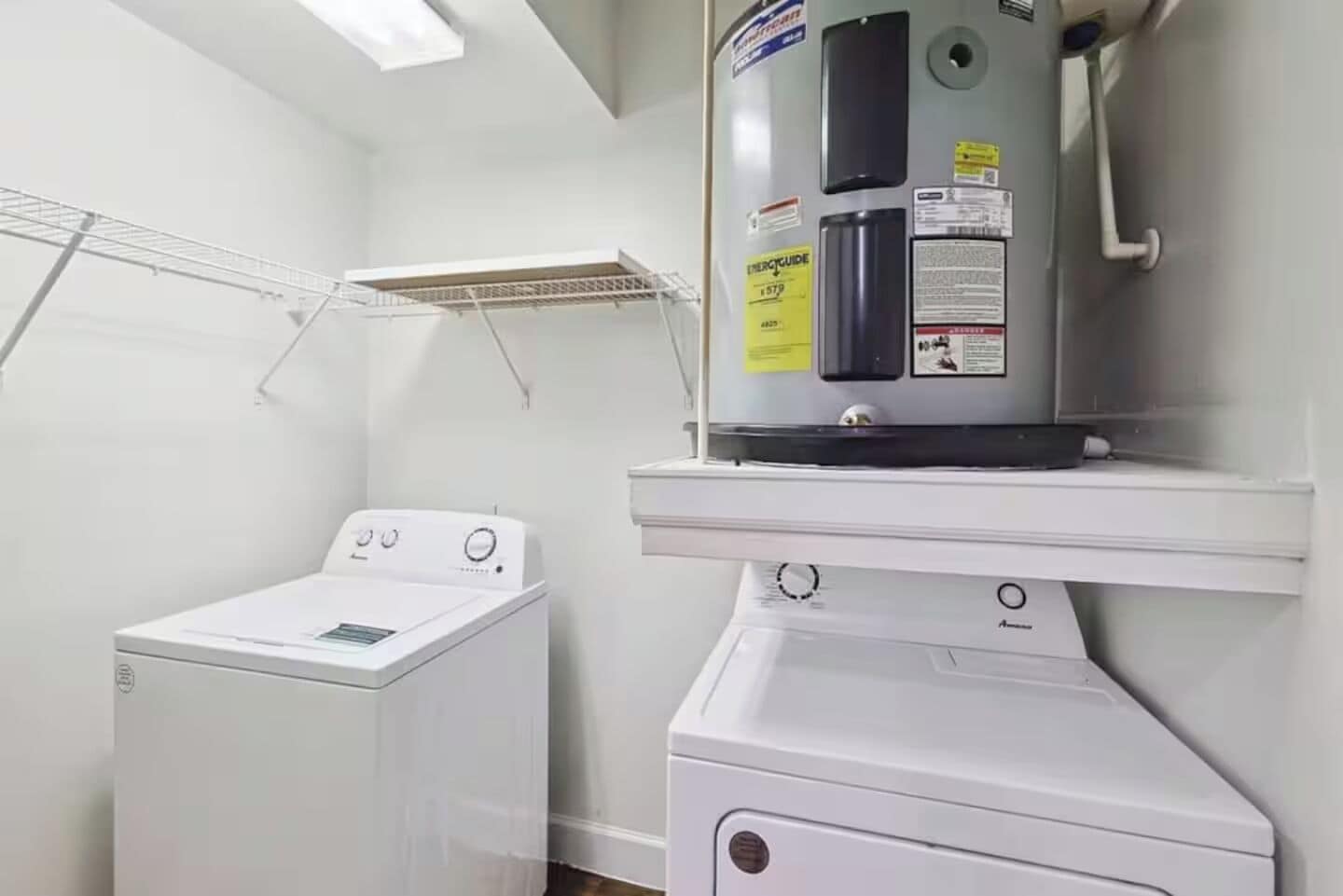 Ein Waschraum mit einer Waschmaschine und einem Trockner, einem Wäscheständer und einem Warmwasserbereiter auf einem Regal.