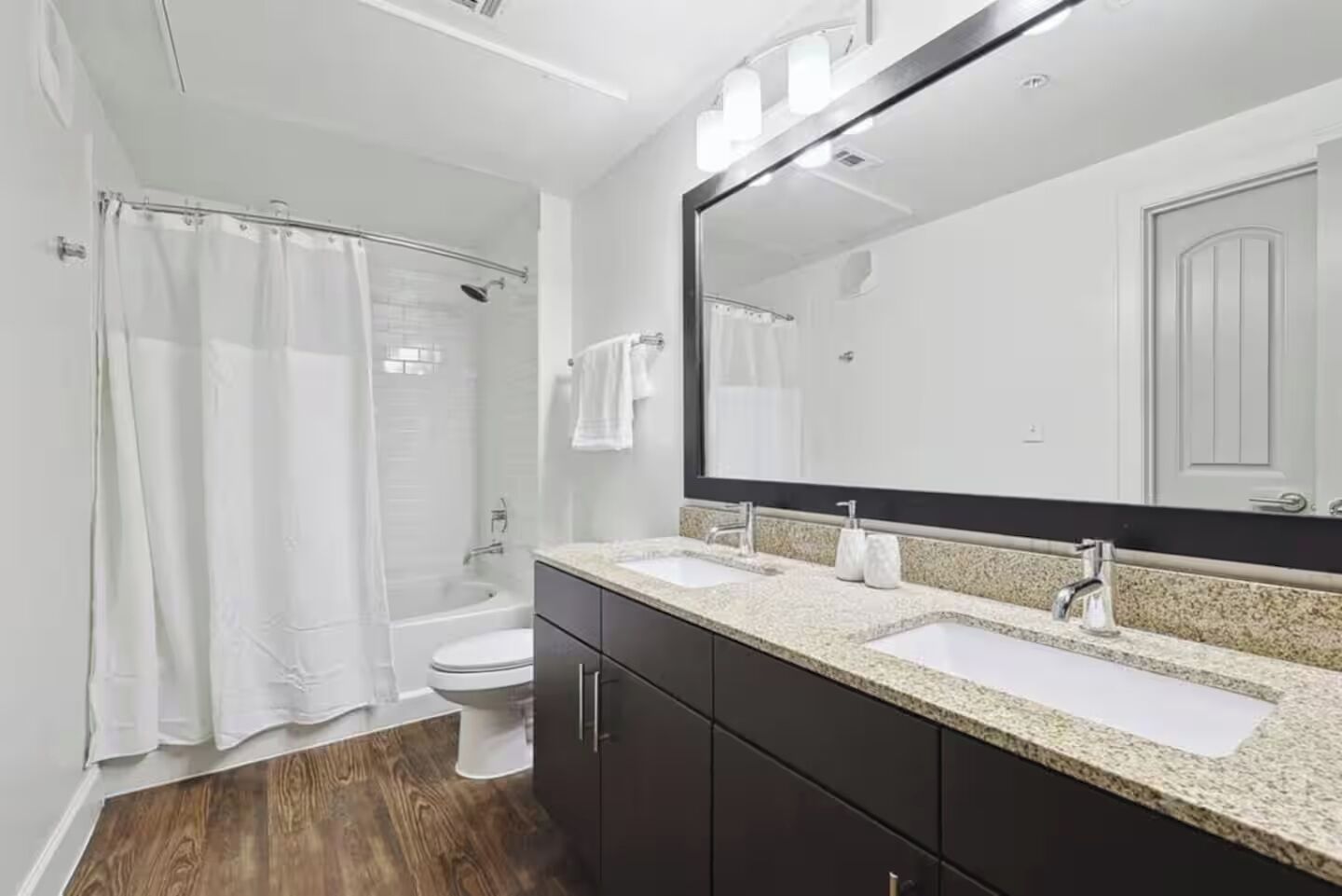A modern bathroom with a shower, toilet, and dual sinks with a large mirror.