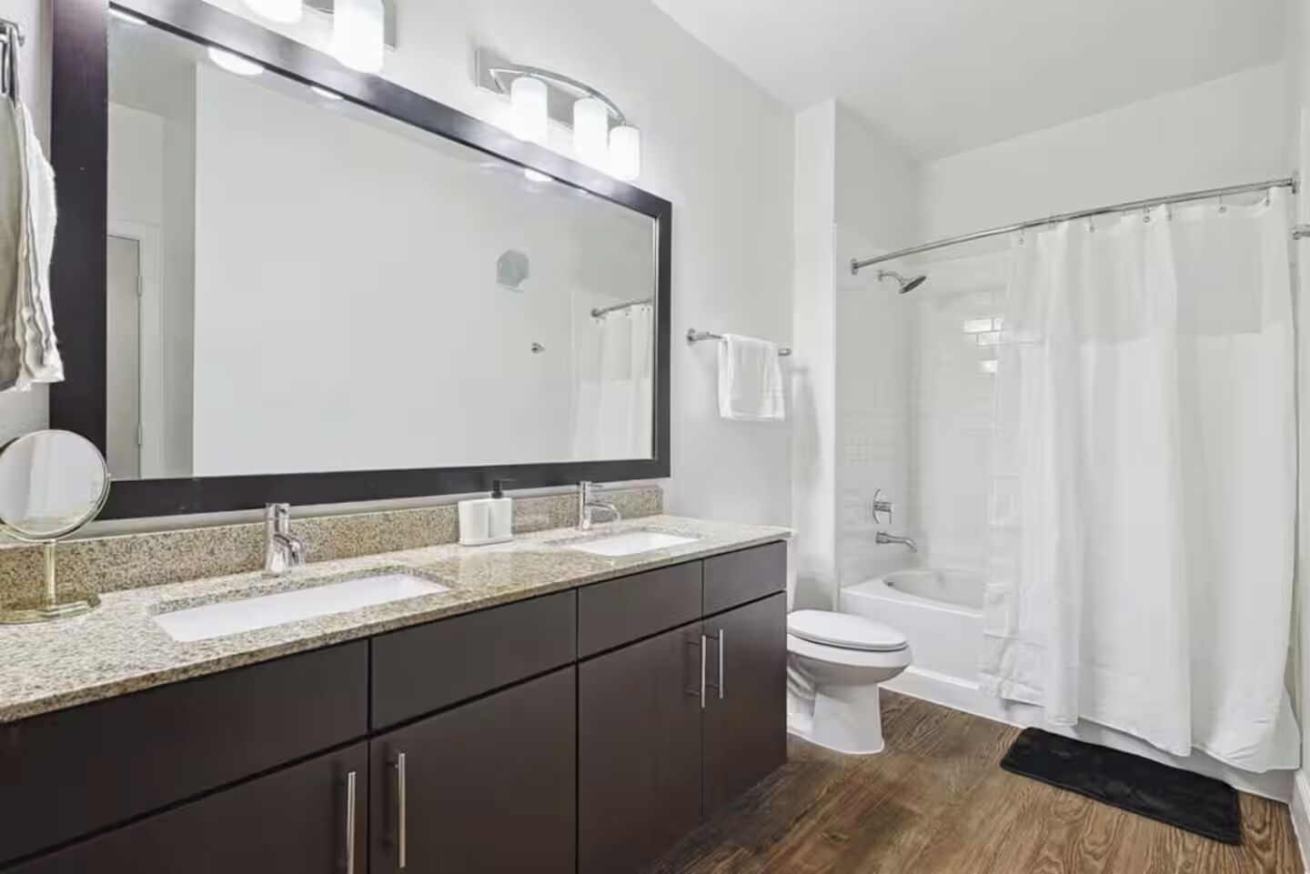 A modern bathroom with a double sink vanity, a large mirror, a toilet, and a shower area.
