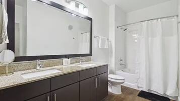 A modern bathroom with a double sink vanity, a large mirror, a toilet, and a shower area.